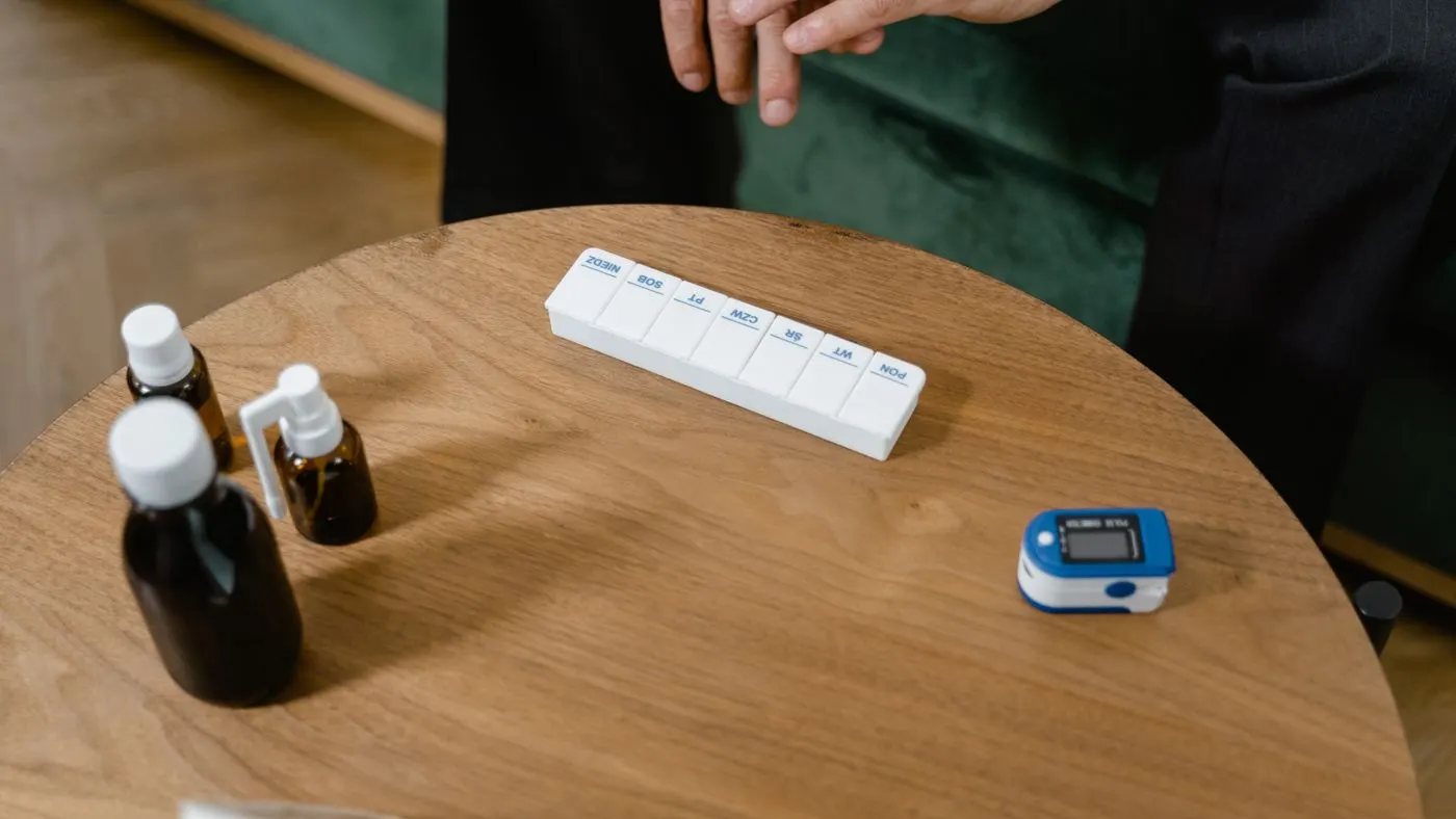 Pastillero semanal, frascos de medicina y un oxímetro de dedo sobre una mesa redonda de madera