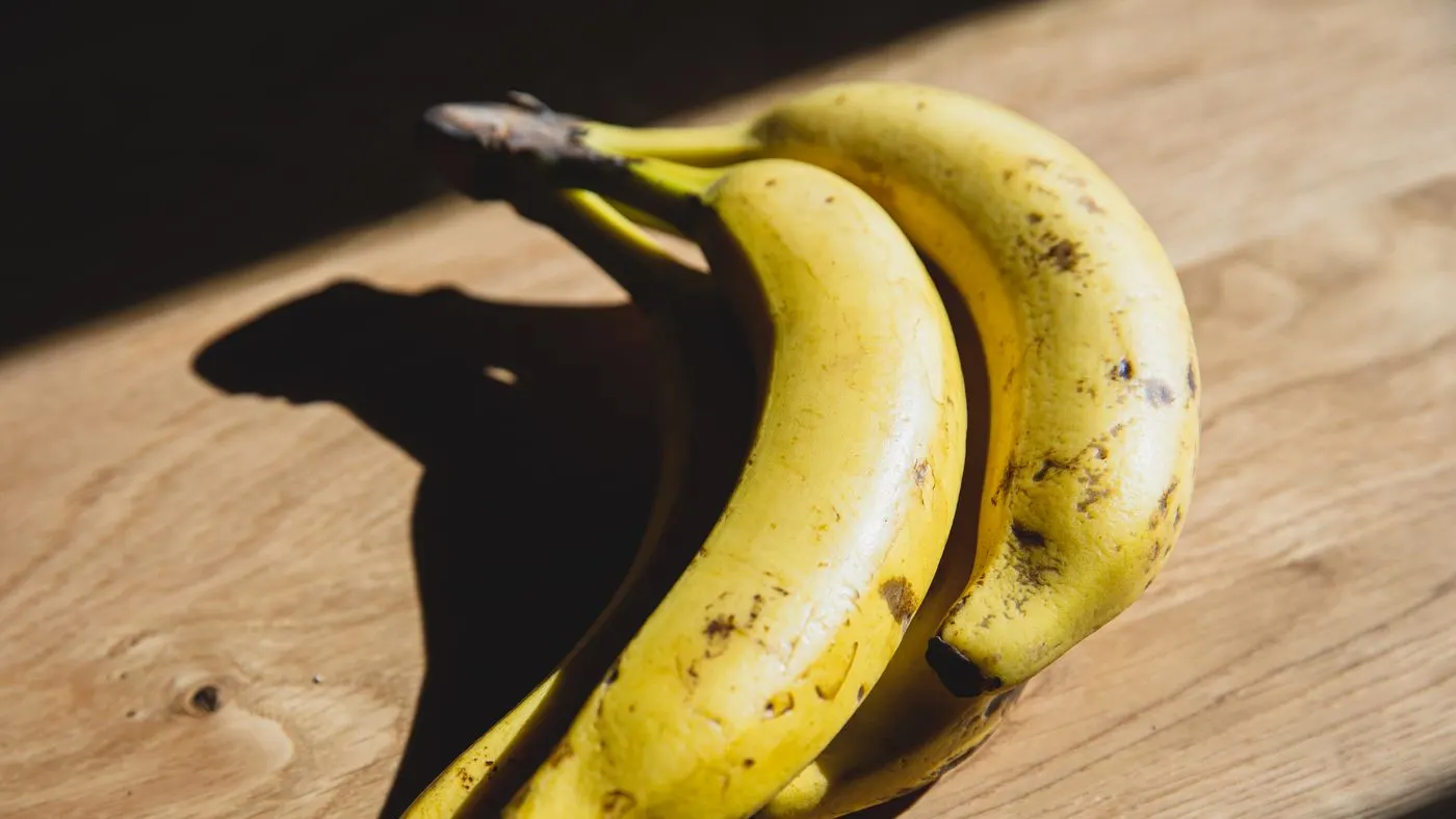 Dos bananos maduros sobre una mesa de madera con el sol entrando de lado, imagen para la guía de la espironolactona y el potasio