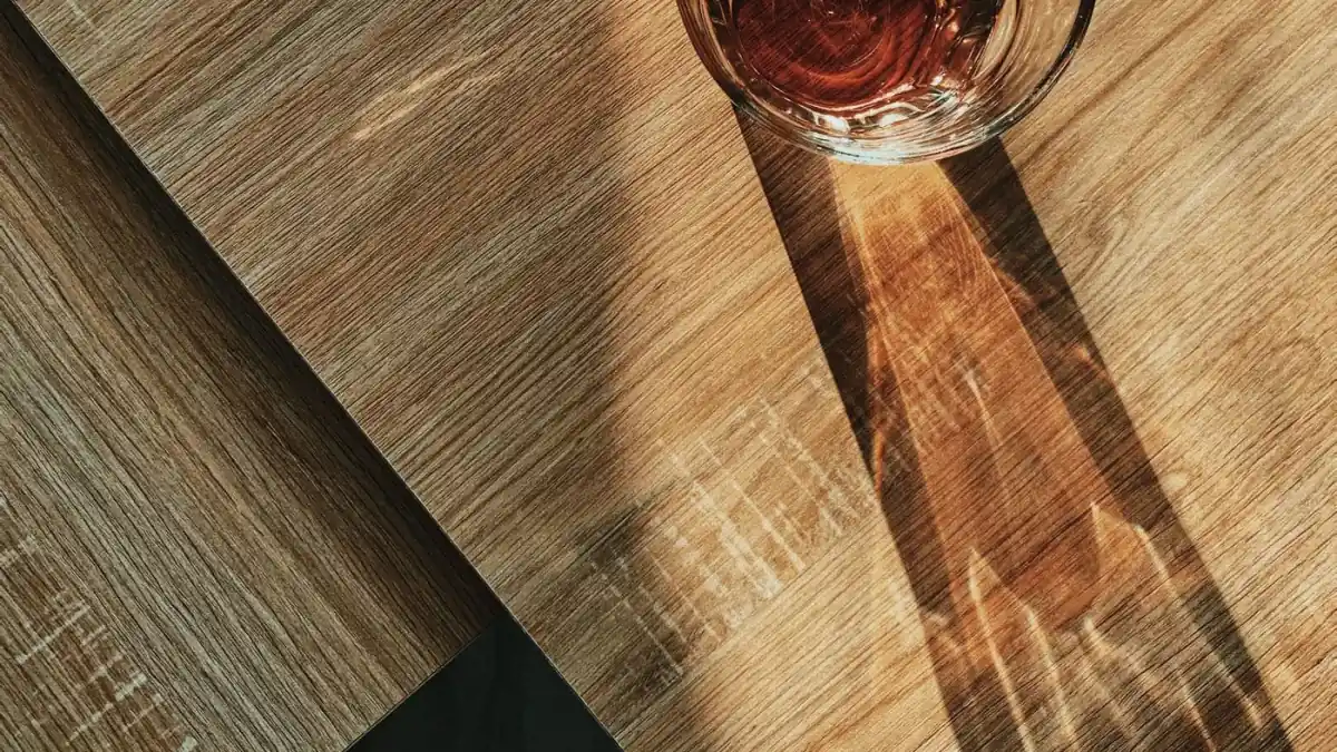 Vaso con una bebida rojiza sobre una mesa de madera, con la sombra que deja el sol entrando de lado, imagen para la guía de la furosemida